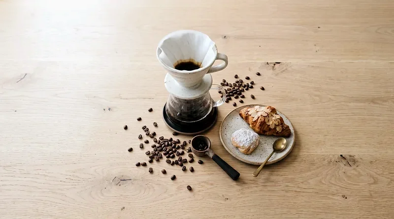 Derselbe Filterkaffee mit Kaffeebohnen und Gebäck auf dem Holztisch, mit kühlerer Farbbalance, weicheren Lichtern und schärferen Details.